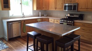 A modern kitchen with wooden cabinets, stainless steel appliances, a central island with bar stools, and a dishwasher. - Ski In/Out, Walk To Trails & Town, 4 Bdr Townhome. (Breckenridge)