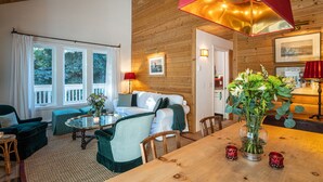Ett mysigt rum med ett träpanelat tak, en vit soffa, ett glasbord och ett matbord med en vas med blommor.