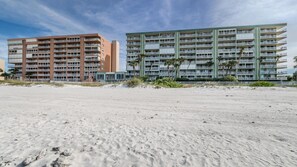 Ein Sandstrand mit zwei mehrstöckigen Gebäuden im Hintergrund.