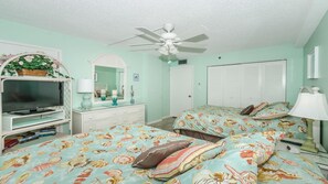 Ein Schlafzimmer mit zwei Betten, einem Fernseher, einem Schminktisch und einem Deckenventilator.