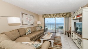Ein Wohnzimmer mit einer Couch, einem Couchtisch und einer TV-Konsole. Ein Balkon bietet Blick auf das Meer.