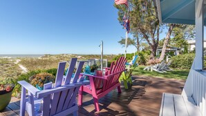 A deck with colorful Adirondack chairs, a flag, and a view of the ocean. - Beachfront, Chic a si Cottage, original vintage Florida charm right on the Gulf (Indian Rocks Beach)