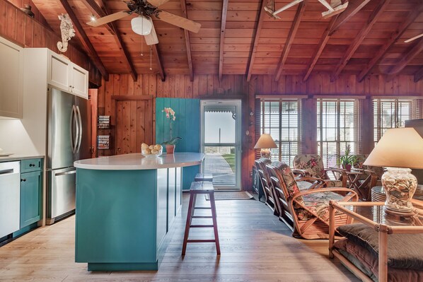 A kitchen with a central island, wooden ceiling, and a dining area with wicker chairs. - Beachfront, Chic a si Cottage, original vintage Florida charm right on the Gulf (Indian Rocks Beach)