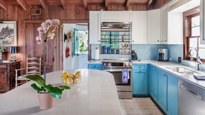 A kitchen with wooden beams, a large island with a plant, and a view of the outdoors. - Beachfront, Chic a si Cottage, original vintage Florida charm right on the Gulf (Indian Rocks Beach)