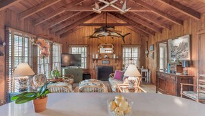 A wooden cabin interior with a dining table, chairs, a television, and a fireplace. - Beachfront, Chic a si Cottage, original vintage Florida charm right on the Gulf (Indian Rocks Beach)
