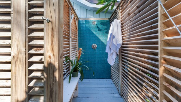 A narrow wooden pathway leading to a blue-tiled shower area with a white towel hanging on the wall. - Beachfront, Chic a si Cottage, original vintage Florida charm right on the Gulf (Indian Rocks Beach)