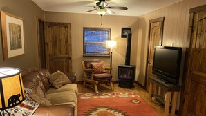 A cozy living room with a leather couch, a wooden rocking chair, a fireplace, a television, and a ceiling fan. - Quiet vacation house on forested property in Ouray (Ouray)