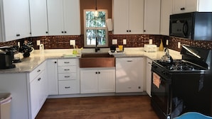 A modern kitchen with white cabinets, a stainless steel range, and a window with a view of trees. - Quiet vacation house on forested property in Ouray (Ouray)
