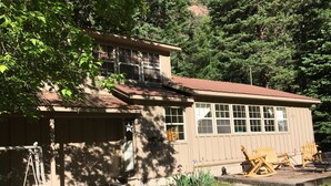 A two-story building with a red roof, a covered porch, and a small garden area with chairs and plants. - Quiet vacation house on forested property in Ouray (Ouray)