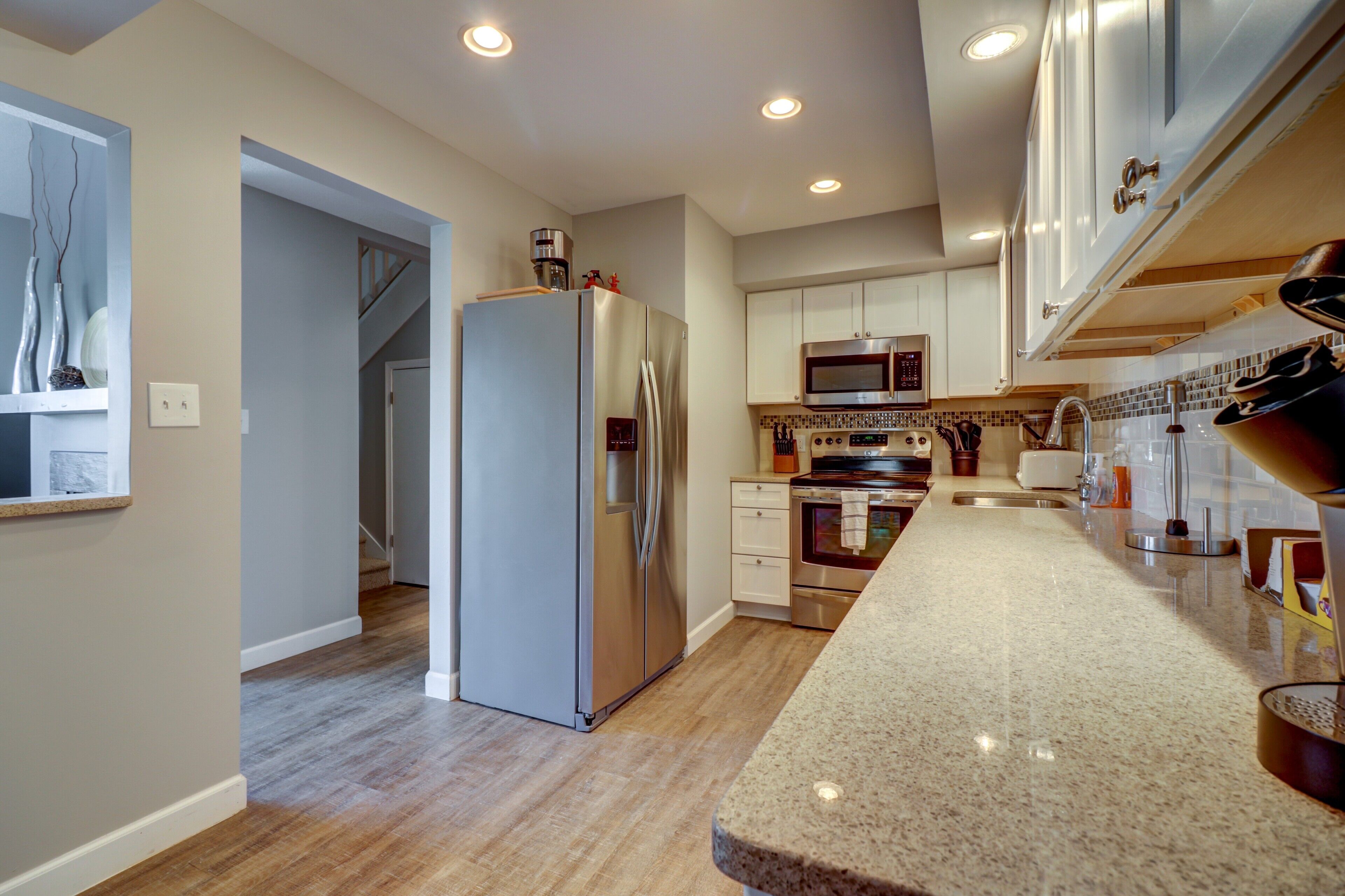A modern kitchen with stainless steel appliances, a wooden floor, and a granite countertop.