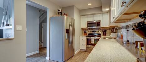 A modern kitchen with stainless steel appliances, a wooden floor, and a granite countertop.
