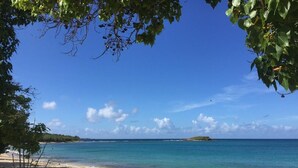 A beach with clear turquoise water, a sandy shore, and a small island in the distance. - Gorgeous, Spa-like 3BR with Island Elegance & Stunning Ocean Views (St Thomas)