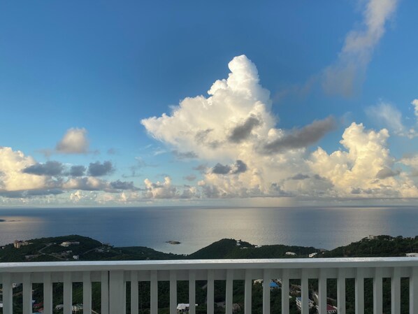 A coastal view with a white railing, a calm sea, and scattered clouds.
