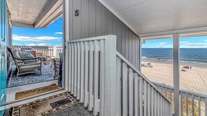 A balcony with a wicker chair and a rug, overlooking a beach with people and umbrellas. - Come on down! Great weather, comfortable furniture and beds! 
Best view! (Surfside Beach)