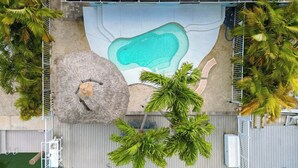 An aerial view of a pool area with a thatched roof structure, palm trees, and a green artificial turf surface. - A Cut Above - 5 Star property that lives up to its name (Key Colony Beach)