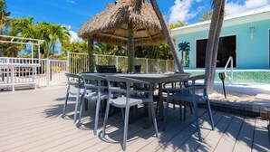 A deck with a table and chairs, a thatched-roof structure, a pool, and a building with the number 191. - A Cut Above - 5 Star property that lives up to its name (Key Colony Beach)