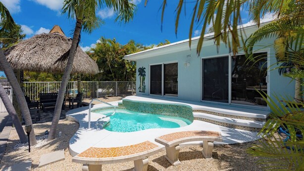 A pool area with a thatched roof, palm trees, and a building with large windows. - A Cut Above - 5 Star property that lives up to its name (Key Colony Beach)