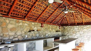 A kitchen with a stone wall, a wooden ceiling, and a bar area with stools. - Casa Torote, La Ventana (El Sargento)