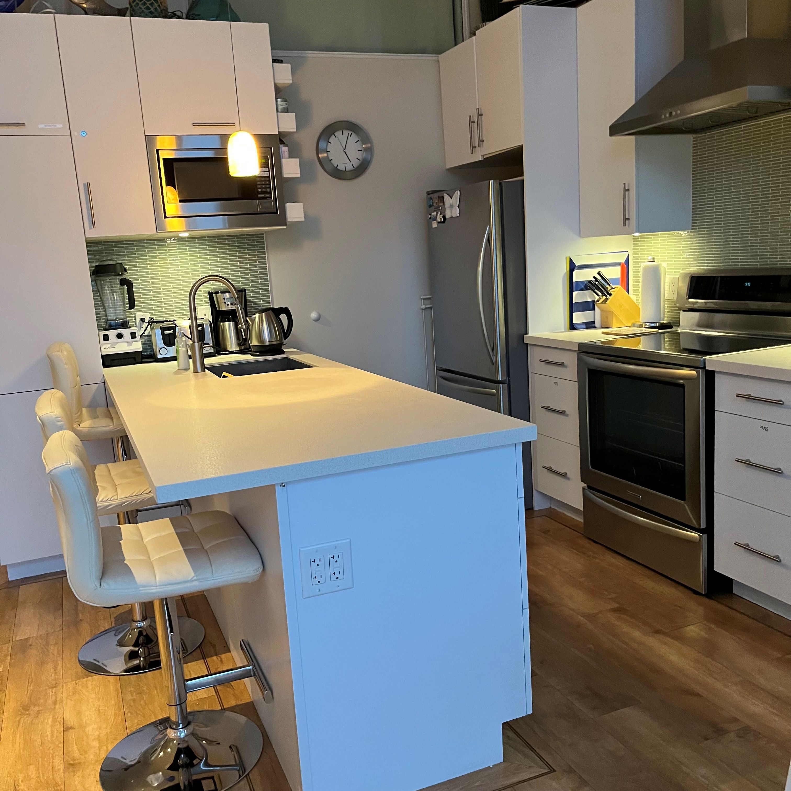 Een moderne keuken met een centraal eiland, roestvrijstalen apparatuur en een klok aan de muur.
