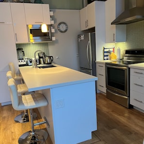 A modern kitchen with a central island, stainless steel appliances, and a clock on the wall.