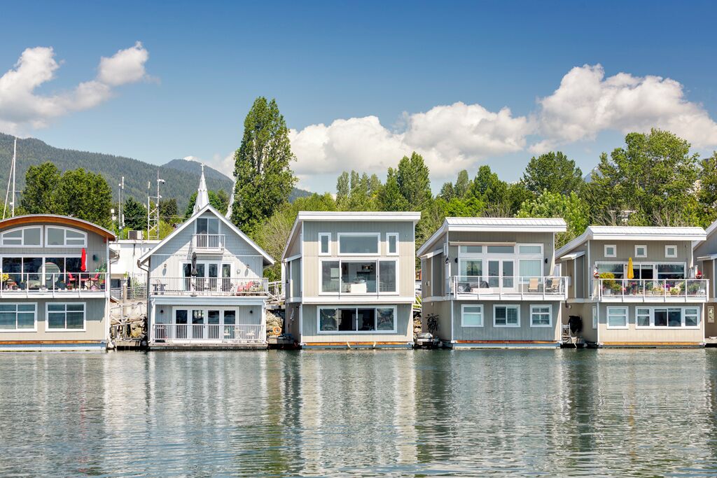 Une rangée de maisons flottantes dotées de plusieurs terrasses, de grandes fenêtres et, en arrière-plan, une étendue d’eau calme.