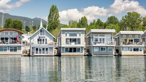 Une rangée de maisons flottantes dotées de plusieurs terrasses, de grandes fenêtres et, en arrière-plan, une étendue d’eau calme.