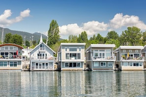 A row of floating houses with multiple decks, large windows, and a calm water body in the background.