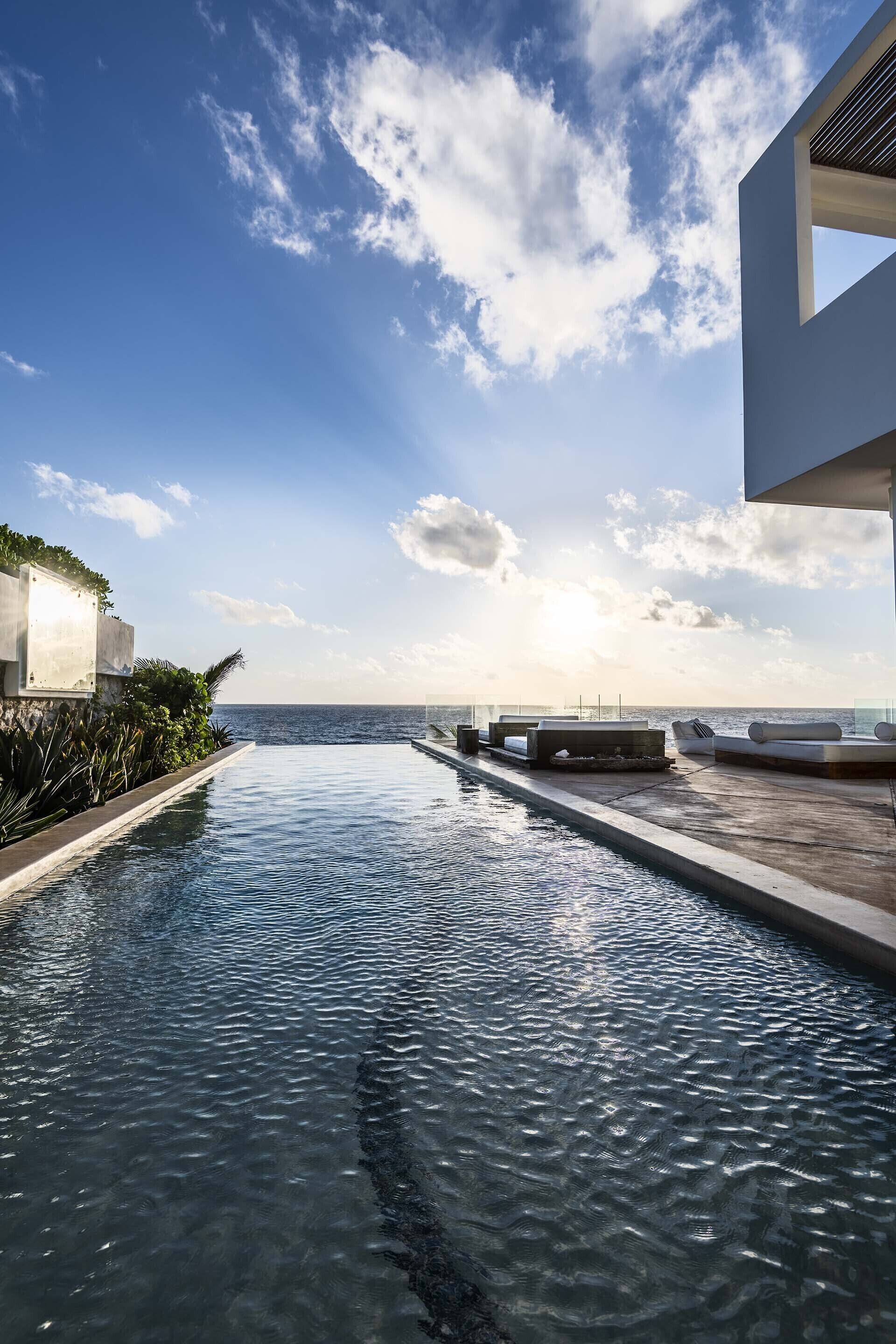 A pool with a view of the ocean, a modern building, and a clear sky.