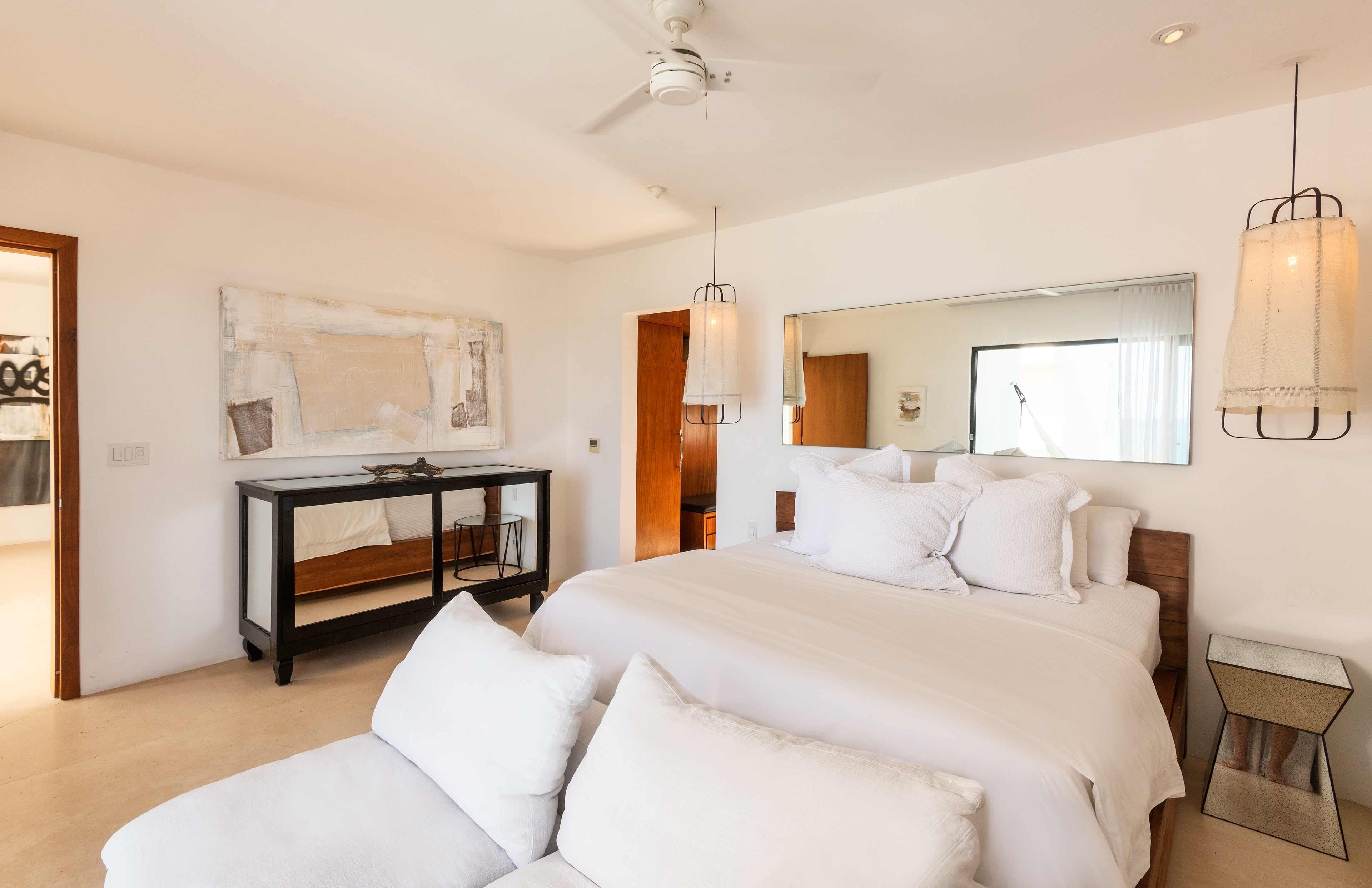 A modern bedroom with a large bed, bedside tables, a mirror, and a ceiling fan.