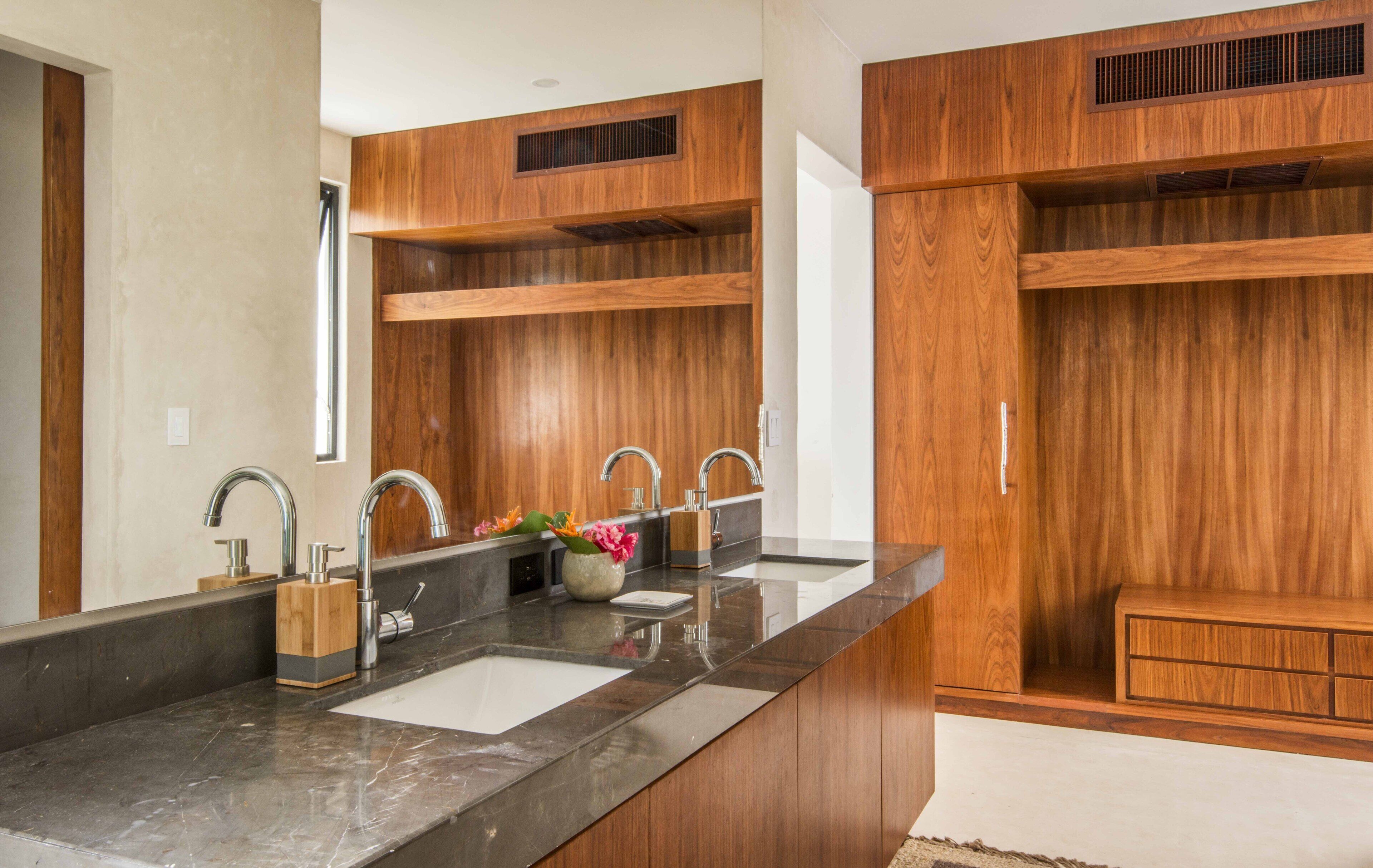 A modern bathroom with a large vanity, two sinks, and wooden cabinetry.