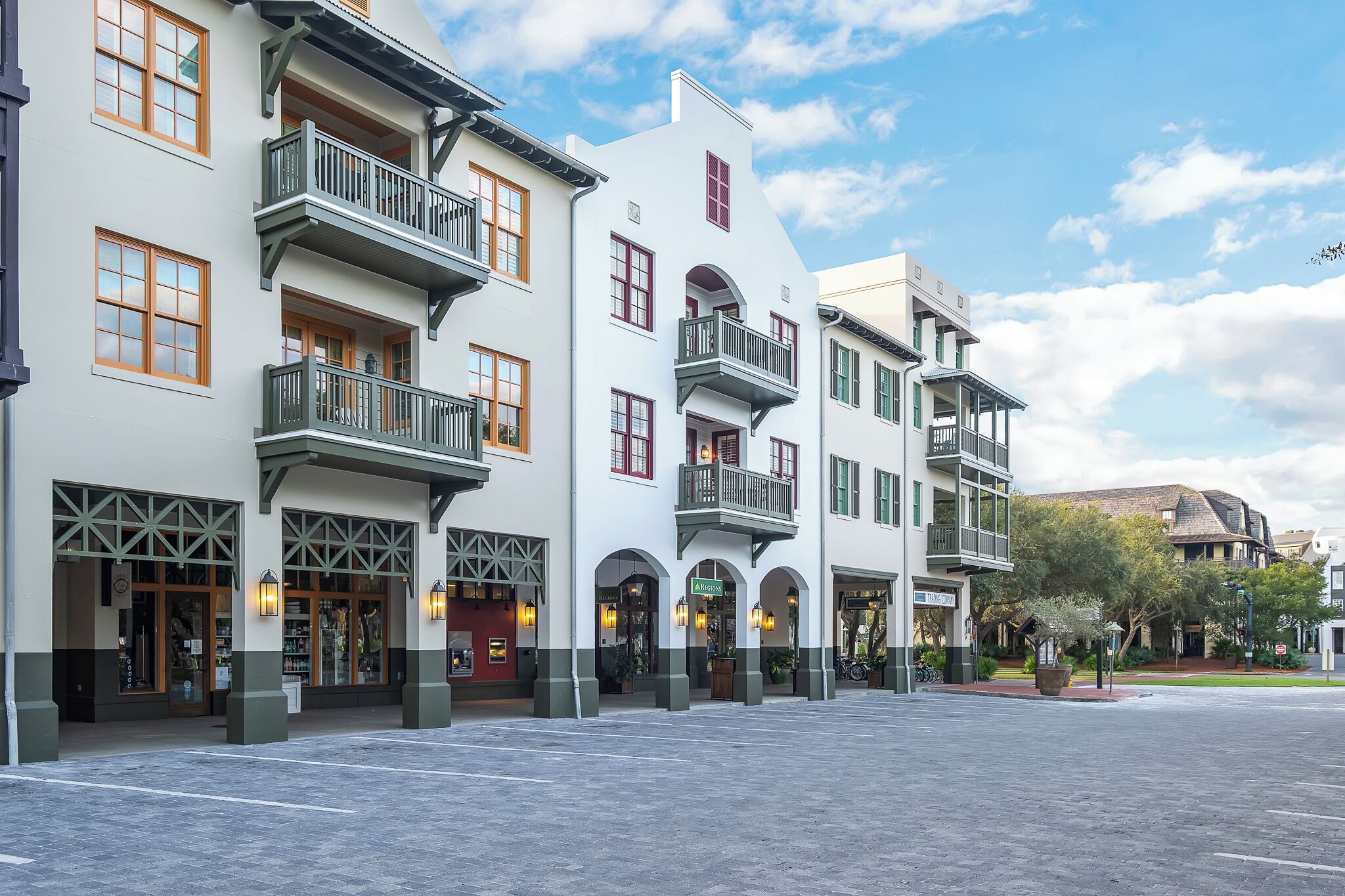 Una hilera de edificios blancos con detalles verdes y múltiples balcones, con ventanas amplias y un arco central.