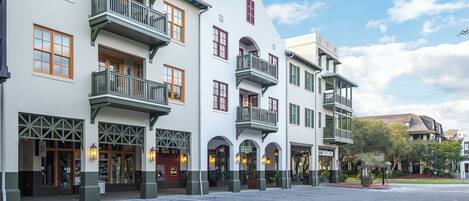 A row of white buildings with green trim and multiple balconies, featuring large windows and a central archway.