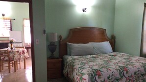 A bedroom with a bed, nightstand, lamp, and a small table with a vase. - Antigua Seaview Alamanda 6 - Affordable, Convenient And Comfortable (St. John's)