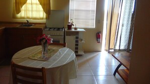 A small kitchen with a stove, sink, and a dining table with chairs. There is a window with blinds and a fire extinguisher mounted on the wall. - Antigua Seaview Alamanda 6 - Affordable, Convenient And Comfortable (St. John's)