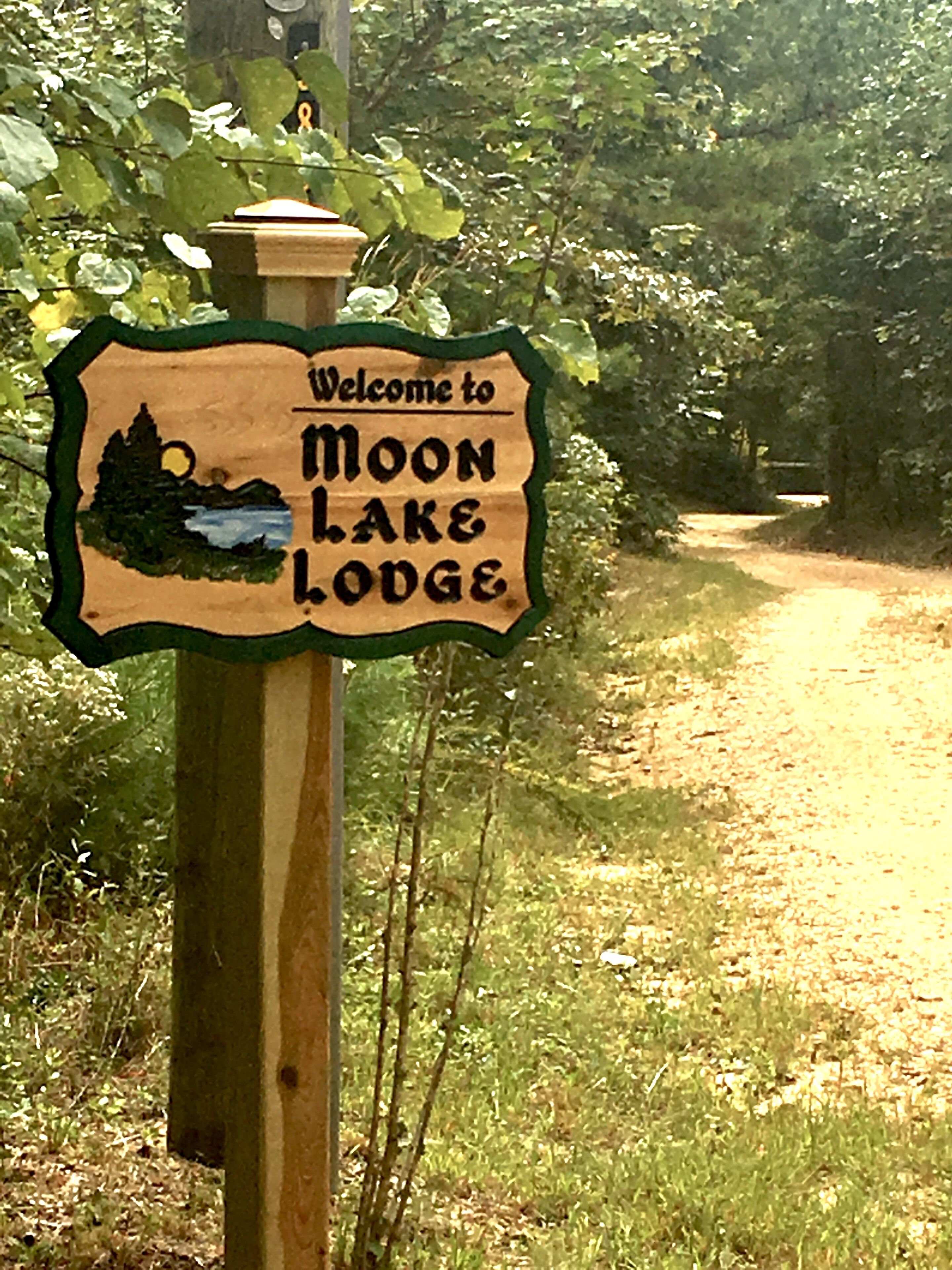 A wooden sign with a welcome message to Moon Lake Lodge.