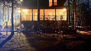 Une cabane en bois à deux étages, dotée de grandes fenêtres, d’un porche couvert et d’un escalier menant à l’entrée.