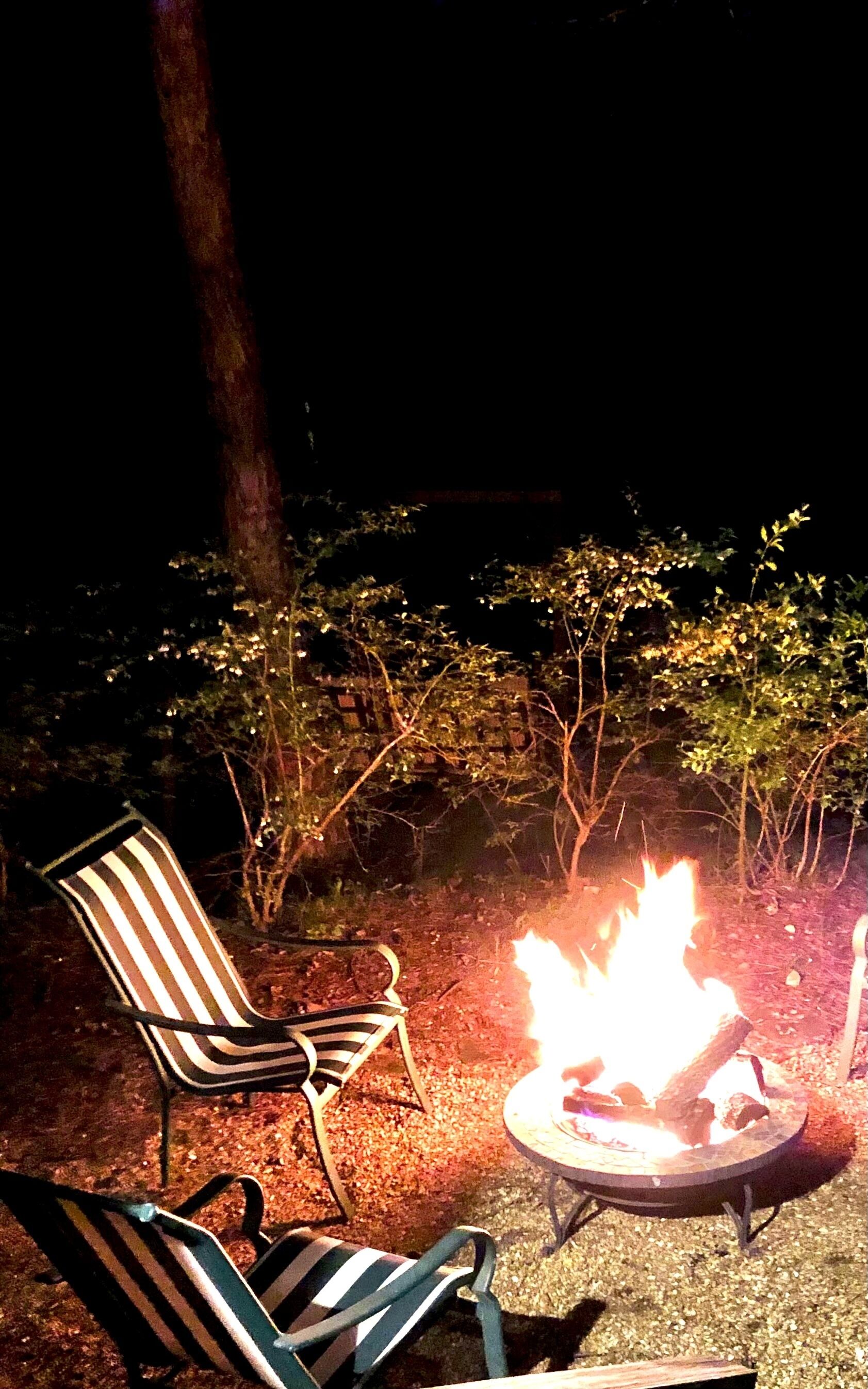 A nighttime outdoor seating area with a fire pit and two striped chairs.