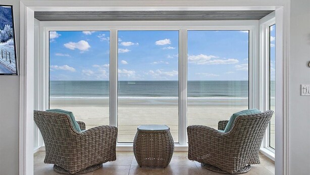 Ein Zimmer mit großem Fenster und Meerblick, ausgestattet mit Korbmöbeln und einem kleinen runden Tisch.
