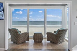 Ein Zimmer mit großem Fenster und Meerblick, ausgestattet mit Korbmöbeln und einem kleinen runden Tisch.
