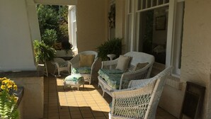 A covered patio area with wicker furniture, a tiled floor, and potted plants.