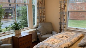 A bedroom with a large bed, a chair, a dresser, and a window with curtains.