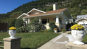A two-story house with a front porch, surrounded by a well-maintained lawn and a mountain backdrop.