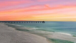 A beach with a pier extending into the ocean, clear skies, and calm waters.