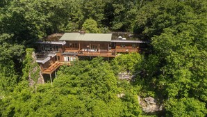 Un grand chalet à plusieurs étages, doté d’un toit végétalisé et entouré d’une forêt dense.