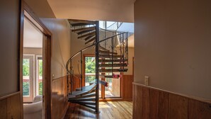 Un intérieur en bois avec un escalier en colimaçon, une porte donnant sur un espace extérieur et une vue sur la verdure.