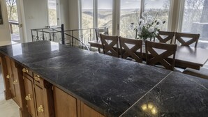 Une cuisine dotée d’un plan de travail en marbre noir, de meubles de rangement en bois et d’un coin repas avec des chaises et une table en bois.