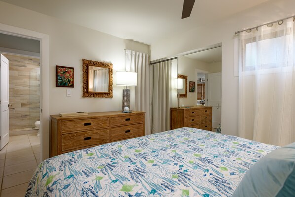 A bedroom with a bed, wooden dresser, mirror, and a bathroom door.