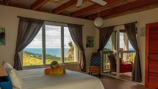 Un dormitorio con cama, vistas al océano y un balcón con sillas.