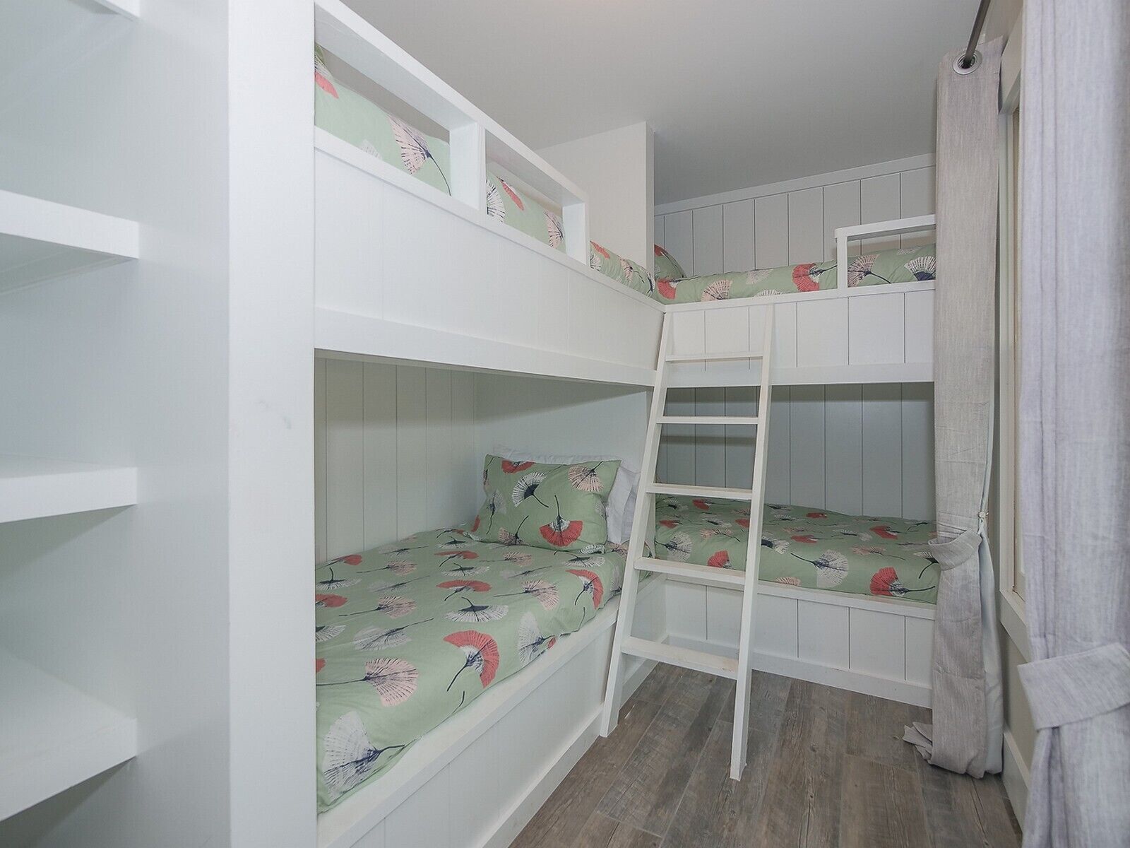 A bunk bed room with a ladder, white walls, and a wooden floor.