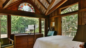 Un dormitori de cabana de fusta amb un llit, una banca de fusta, un taulell de nit i una finestra amb vitralls de colors.
